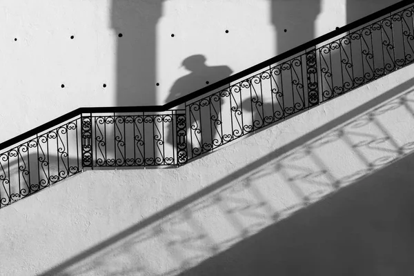 Staircase with black banister against white wall, with shadows. Stock Photo