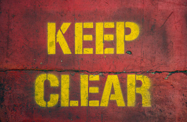 Worn and grungy Keep Clear sign stenciled on concrete.