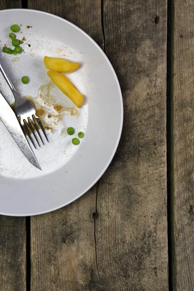 Overhead shot of an empty plate with leftovers from a meal on a rustic wooden background — Stock Photo, Image