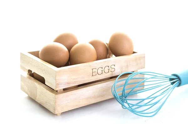 卵の白い背景の上のオレンジ色の卵泡立て器で木製の箱 — ストック写真