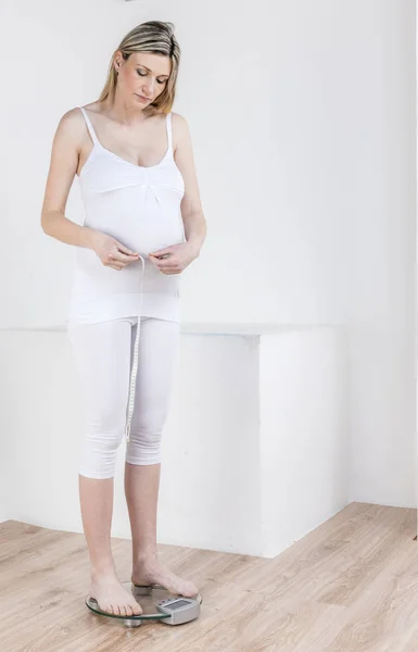 怀孕的女人站在体重秤用卷尺测量 — 图库照片
