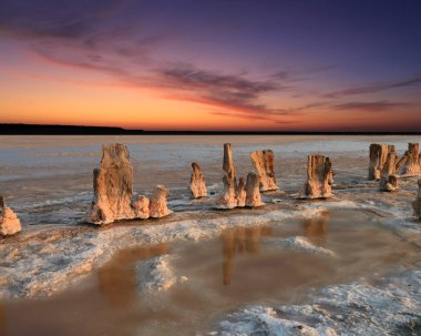 Kızıl gökyüzü günbatımı arka planında tuz gölünde eski tahta direkler