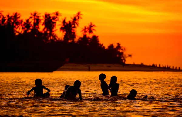 Silhouetten von Kindern, die bei Sonnenuntergang im Wasser spielen — Stockfoto