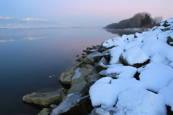 Piedras en la nieve en la orilla del lago de montaña — Foto de Stock