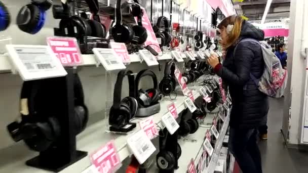 Jovem escolhe fones de ouvido na loja de eletrônicos — Vídeo de Stock