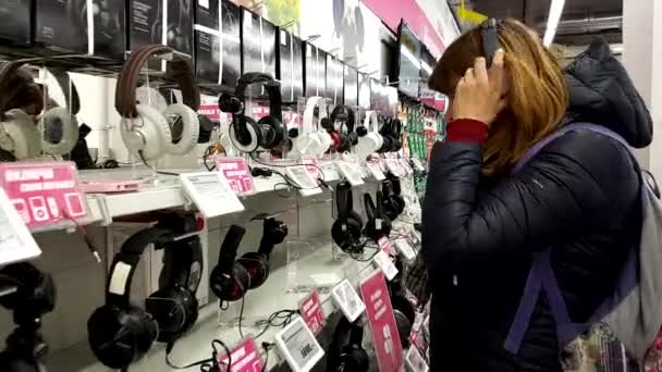 Mujer joven elige los auriculares en la tienda de electrónica — Vídeos de Stock