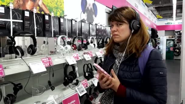 Mujer joven elige los auriculares en la tienda de electrónica — Vídeo de stock