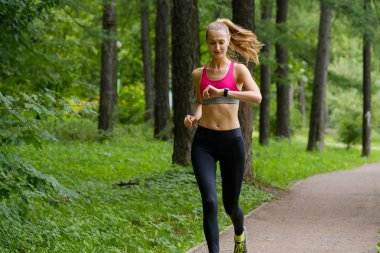 Genç bir kadın parkta koşuyor.