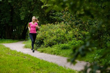 Genç bir kadın parkta koşuyor.
