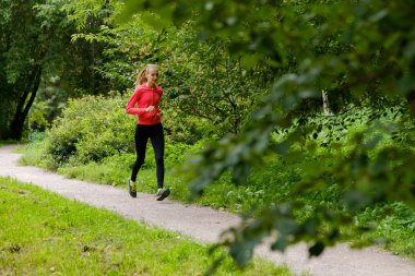 Genç bir kadın parkta koşuyor.