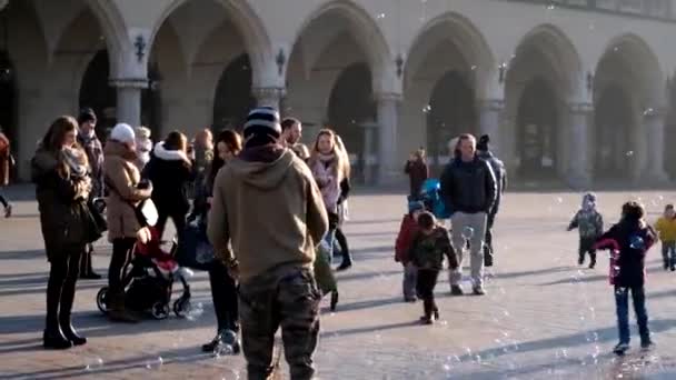 Young man blowing bubbles, happy tourists and children playing with them — Stock Video