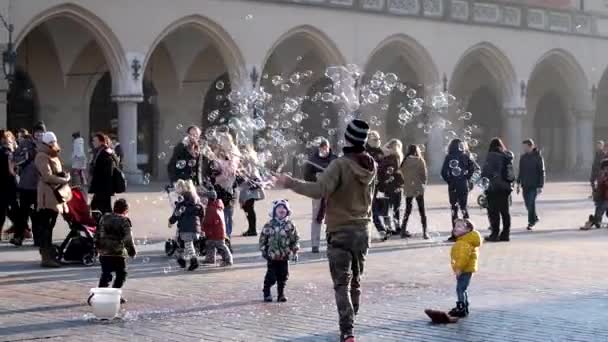 Young man blowing bubbles, happy tourists and children playing with them — Stock Video