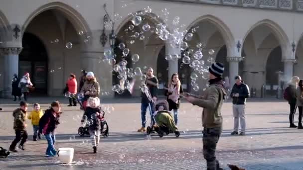 Jonge man waait bubbels, gelukkig toeristen en kinderen spelen met hen — Stockvideo