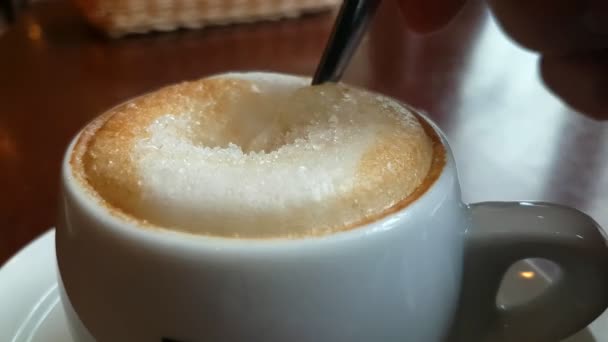 Ложка перемешивает сахар в чашке с капучино — стоковое видео