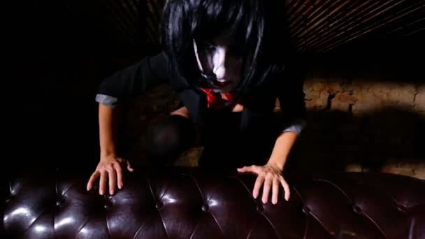 Девушка с макияжем в кошмарном стиле вылезает из-за кожаного дивана — стоковое видео