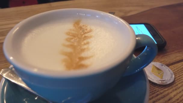 Capuchino y moneda etéreo sobre la mesa en el panorama cafetería de izquierda a derecha . — Vídeo de stock