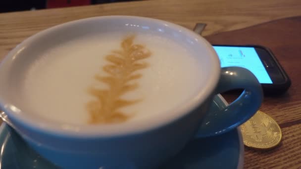 Capuccino und Bitcoin-Goldmünze auf dem Tisch im Café-Panorama von links nach rechts — Stockvideo