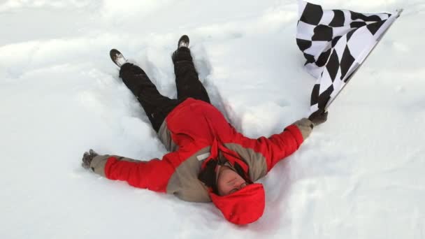 Man ligt in de sneeuw met de finishvlag — Stockvideo