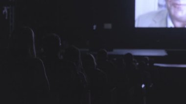 İş konferansına gelen ziyaretçiler ekranda bir sunum izliyor