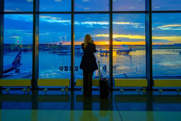 Žena stojí u okna na letišti při západu slunce — Stock fotografie