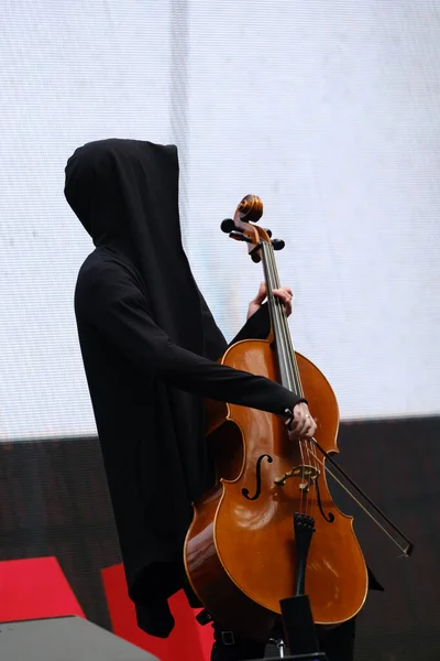 Uomo in vestaglia nera con cappuccio suona il violoncello — Foto Stock