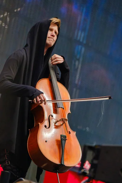 Man i svart rock med huva spelar cello — Stockfoto