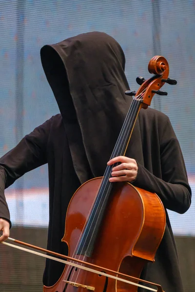 Uomo in vestaglia nera con cappuccio suona il violoncello — Foto Stock