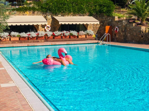 Mujer joven se relaja en la piscina en el juguete inflable flamenco rosa — Foto de Stock