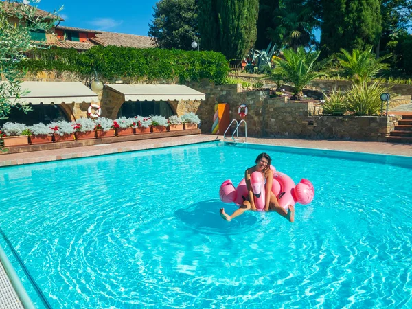 Mujer joven se relaja en la piscina en el juguete inflable flamenco rosa — Foto de Stock