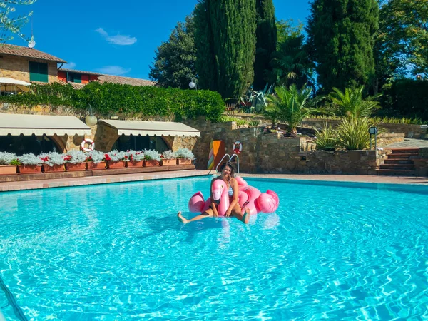 Mladá žena relaxuje v bazénu na nafukovací růžové plameňák hračka — Stock fotografie