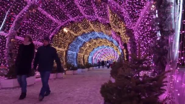 As pessoas andam pelas ruas decoradas com iluminação para o Natal à noite — Vídeo de Stock