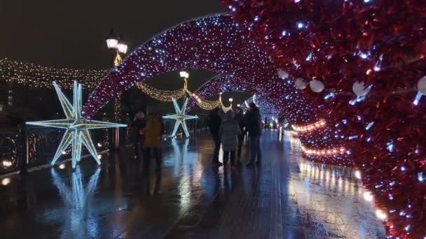 As pessoas andam pelas ruas decoradas com iluminação para o Natal à noite — Vídeo de Stock