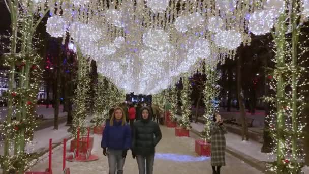 Люди ходять по вулицях, прикрашених освітленням до Різдва ввечері. — стокове відео