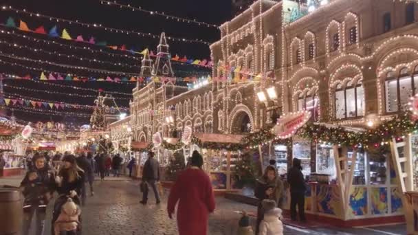 As pessoas andam pelas ruas decoradas com iluminação para o Natal à noite — Vídeo de Stock