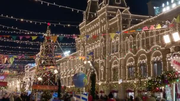 Ludzie chodzą ulicami ozdobione oświetleniem na Boże Narodzenie wieczorem — Wideo stockowe