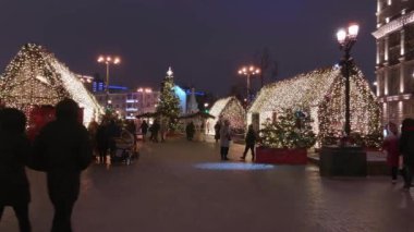 İnsanlar akşamları Noel için aydınlatmalarla süslenmiş şekilde sokaklarda yürür.