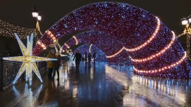 As pessoas andam pelas ruas decoradas com iluminação para o Natal à noite — Vídeo de Stock