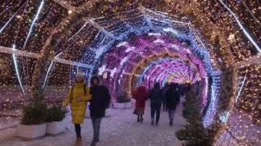 İnsanlar akşamları Noel için aydınlatmalarla süslenmiş şekilde sokaklarda yürür.