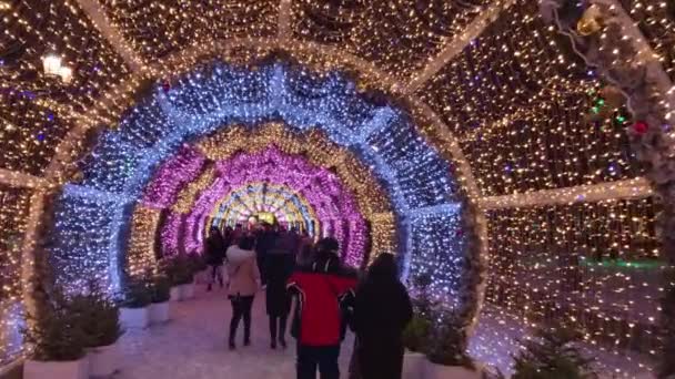As pessoas andam pelas ruas decoradas com iluminação para o Natal à noite — Vídeo de Stock