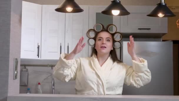 Plus size girl dressed in a bathrobe, curlers on her head, admiring herself in the mirror — Stock Video