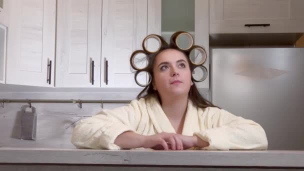 Plus-size meisje gekleed in een badjas, krulspelden op haar hoofd, emotioneel spreekt tot camera — Stockvideo