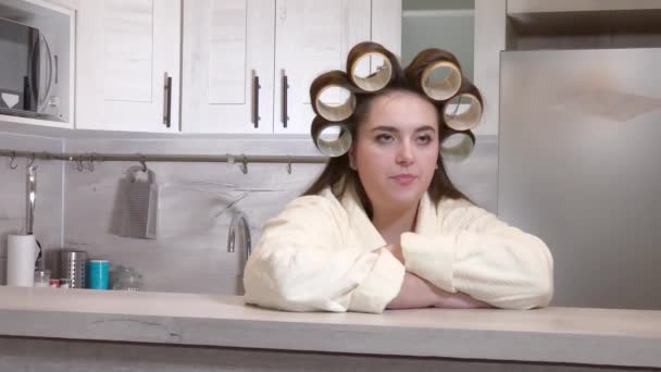 Plus-size girl dressed in a bathrobe, curlers on her head, emotionally speaks to camera — Stock Video