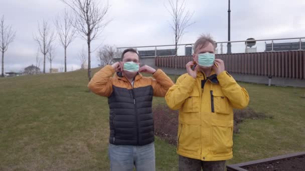 Dos hombres con máscaras médicas están hablando al aire libre. — Vídeos de Stock