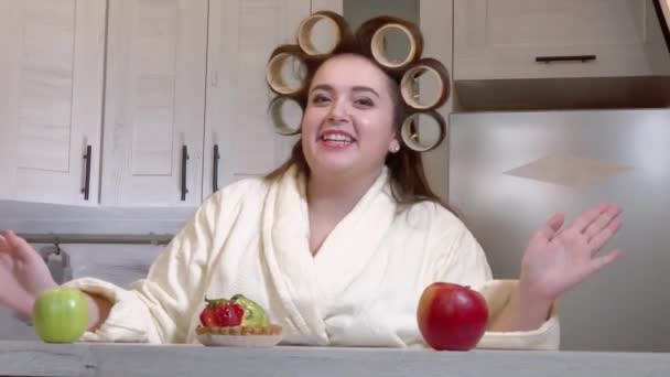 Plus-Size-Mädchen mit Lockenwicklern auf dem Kopf im Bademantel nimmt ein Videoblog auf — Stockvideo