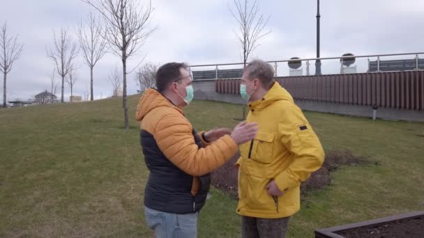 Dos hombres con máscaras médicas están hablando al aire libre. — Vídeos de Stock