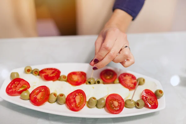Mozzarella peyniri, domates, zeytin ile plaka üzerinde kadın eli.