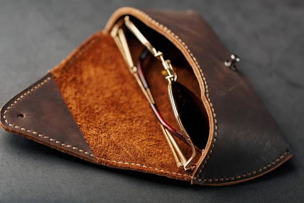Genuine brown leather glasses case, handmade on a dark background. Glasses inside the case