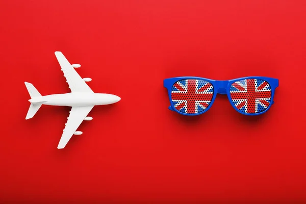 A white passenger plane flies in Sunglasses with the flag of the United Kingdom, on a red background.