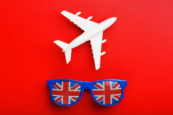 A white passenger plane flies in Sunglasses with the flag of the United Kingdom, on a red background.
