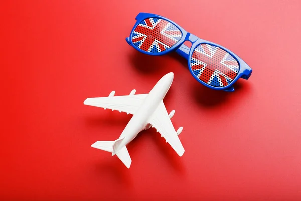 A white passenger plane flies in Sunglasses with the flag of the United Kingdom, on a red background.